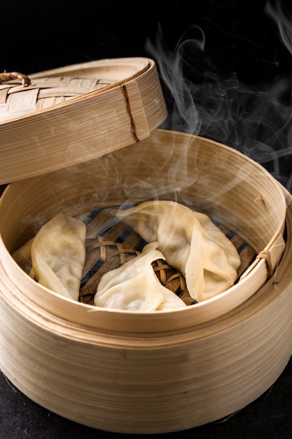 Hot Dumplings lub gyoza podawane w tradycyjnym parowcu na czarnym tle.