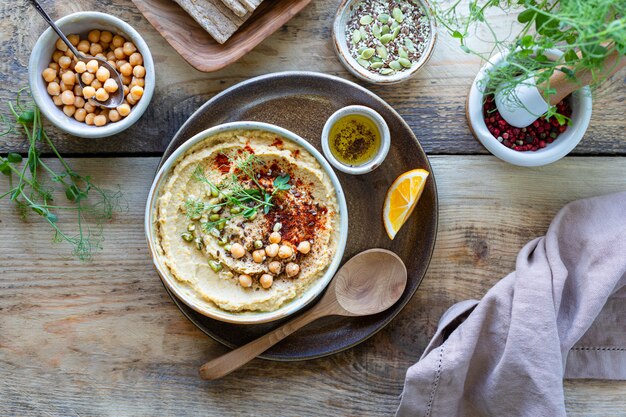 Hummus, sos z ciecierzycy z wędzoną oliwą z papryki w ceramicznej misce na drewnianym tle. Widok z góry.