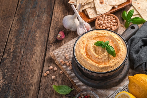 Hummus Z Oliwą Paprykową I Bazylią Z Dodatkami Na Drewnianym Tle