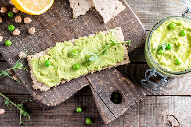 Hummus z zielonego groszku, świeże warzywa, warzywa, krakersy podawane na drewnianej desce, widok z góry, obraz poziomy