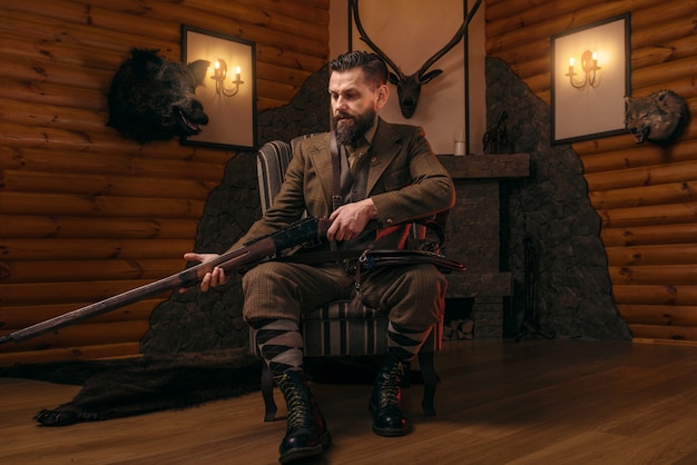 Hunter człowiek w stroju myśliwskim vintage siedzi na krześle z karabinem antycznym.