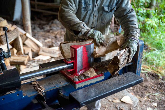 Zdjęcie hydrauliczne ostrze rozdzielające drewno wycina drewno za pomocą robotnika i stosu drewna