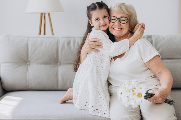 I Love You Granny Portret uroczej dziewczynki uściskającej i całującej babcię w policzek, dającej bukiet kwiatów i pocztówkę, pozdrawiającą kobietę z uroczystością, Dniem Kobiet lub Dniem Matki lub urodzinami