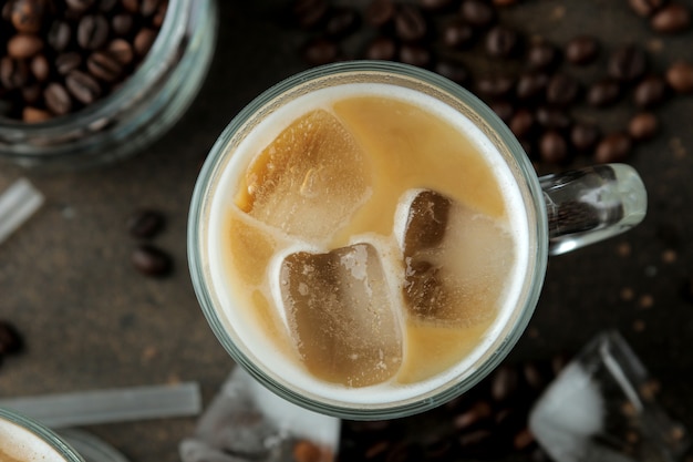 Ice latte lub mrożona kawa z mlekiem i kostkami lodu w szklanej zlewce na ciemnym tle. orzeźwiający napój. letni napój. widok z góry
