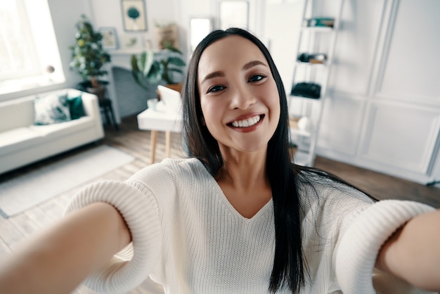 Zdjęcie idealne selfie. atrakcyjna młoda kobieta patrząca w kamerę i uśmiechająca się podczas robienia selfie w domu