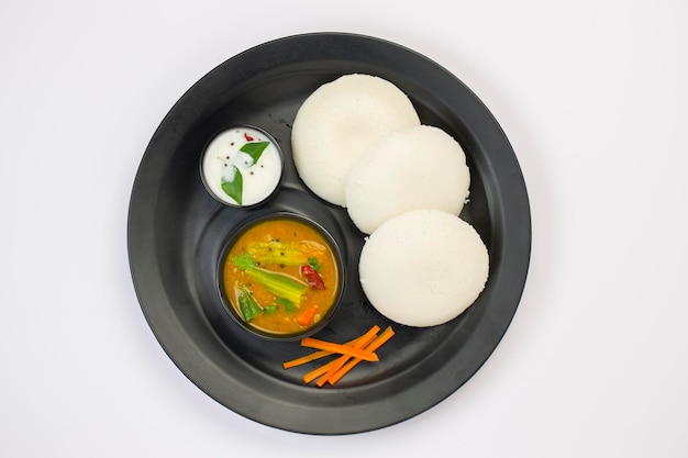 Idly lub Idli South Indian główny produkt śniadaniowy, który jest pięknie ułożony w czarnym talerzu na białym tle