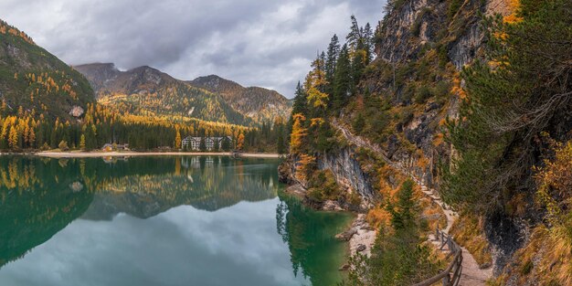 Idylliczne jezioro Braies wczesnym jesiennym rankiem z mgłą unoszącą się nad złotymi modrzewiami