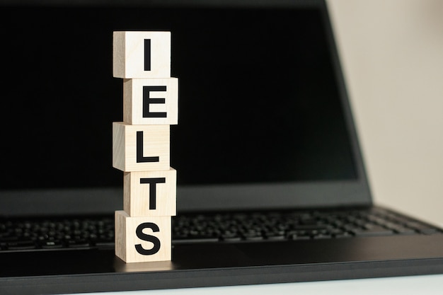 IELTS - skrót od International English Language Testing System - tekst napisany na drewnianym bloku na klawiaturze komputera na tle czarnego