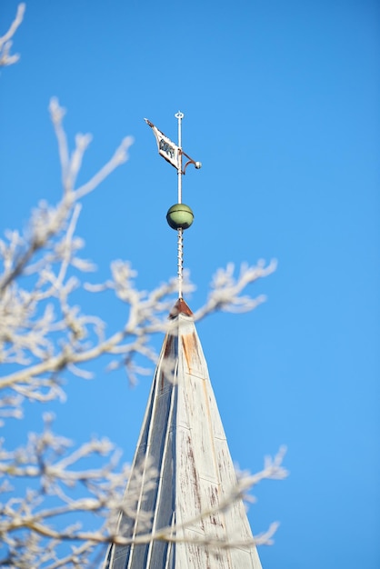 Iglica kościoła nad drzewami Iglica kościoła na tle zachmurzonego nieba na błękitnym niebie Zbliżenie na iglicę w sezonie jesiennym z czystym niebem w tle Gałąź drzewa bez liści