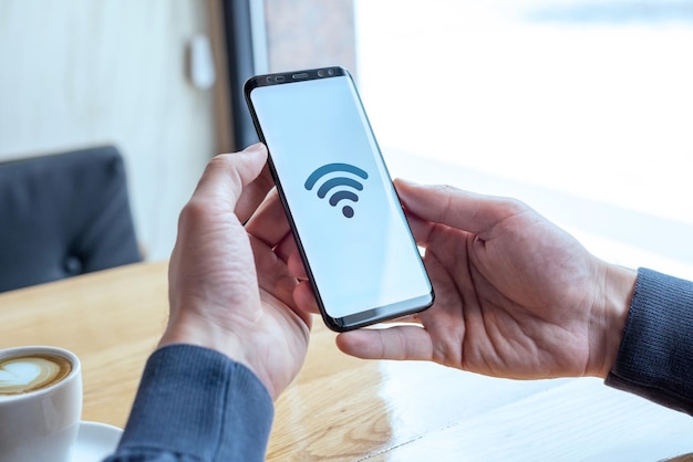 Ikona koncepcji Wi-Fi na wyświetlaczu smartfona Ręce trzymające telefon komórkowy w kawiarni Koncepcja darmowego internetu i globalnego połączenia