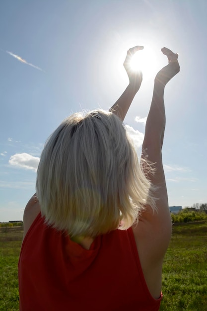 Zdjęcie iluzja optyczna kobiety trzymającej słońce, stojącej na trawie na tle nieba