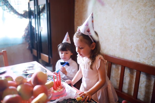 Impreza dzieci w czapkach z okazji urodzin z ciastem i balonami w domu.