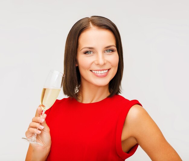 impreza, napoje, święta, koncepcja bożonarodzeniowa - uśmiechnięta kobieta w czerwonej sukience z lampką szampana