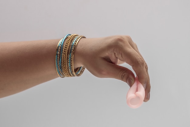 Indianka ręka trzyma krzemowy kubek menstruacyjny wielokrotnego użytku i pokazuje różne rodzaje składania.
