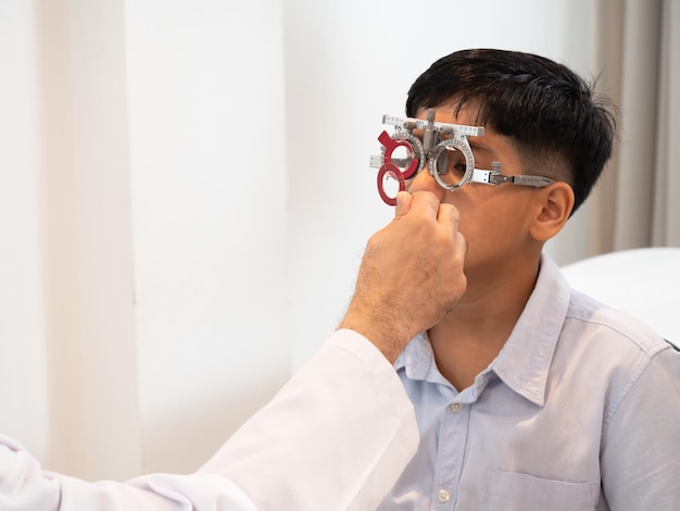 Indie słodki chłopiec siedzący w sklepie z okularami z optometrystą specjalizującym się w chorobach oczu i podstawowym zdrowiu oczu szukającym soczewki pasującej do jego wzroku i uzyskania najskuteczniejszych okularówxA