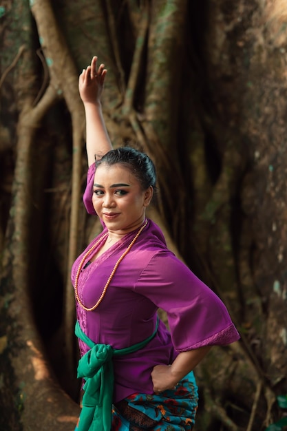 Indonezyjska kobieta odważnie pozuje, unosząc ręce w fioletowej sukience