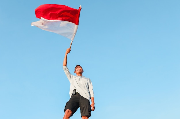 Indonezyjski Mężczyzna Stojący I Machający Indonezyjską Flagą Na Tle Nieba