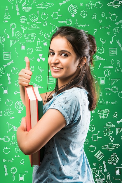 Indyjska azjatycka atrakcyjna studentka trzymająca książki na tle zielonej tablicy z gryzmołami, selektywne skupienie