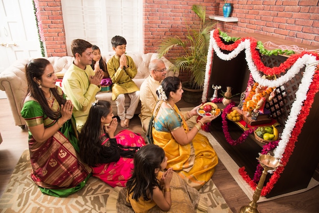 Indyjska azjatycka inteligentna rodzina wykonująca Ganesh puja lub Aarti w domu, nosząc tradycyjne stroje