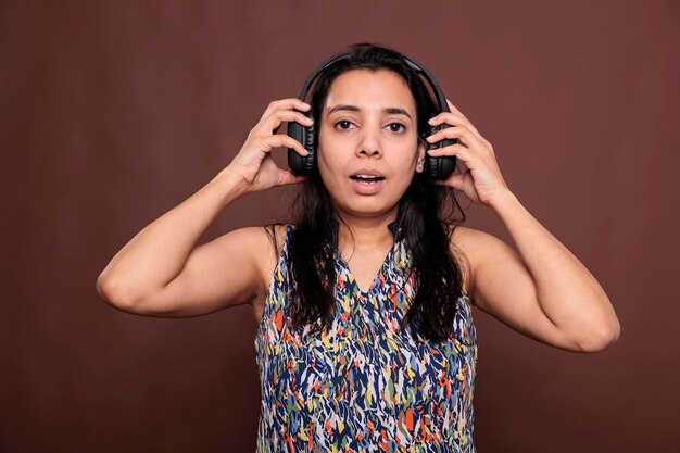 Indyjska kobieta zdejmująca słuchawki bezprzewodowe, patrząca na kamerę ze zdezorientowanym wyrazem twarzy. Pani w słuchawkach, słuchająca portretu piosenki, średnie ujęcie z przodu