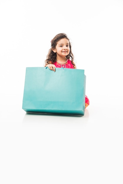 Indyjska mała dziewczynka trzymająca torby na zakupy, stojąca na białym tle nad białym tłem