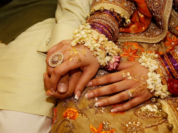 Indyjska pakistańska panna młoda i pan młody siedzą i trzymają się za ręce na imprezie henna mehndi z bliska