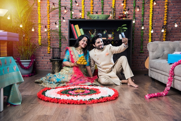 Indyjska Para Robiąca Kwiat Rangoli Na Diwali Lub Onam Festival, Robiąca Selfie Lub Trzymająca Słodycze