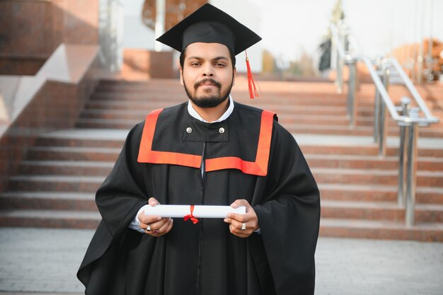 Indyjski absolwent w szacie dyplomowej z dyplomem w przestrzeni kopii kampusu uniwersyteckiego