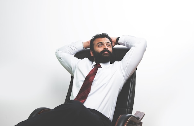 Indyjski azjatycki młody brodaty biznesmen relaksuje się na krześle biurowym z obiema rękami trzymanymi za głową, patrząc w górę