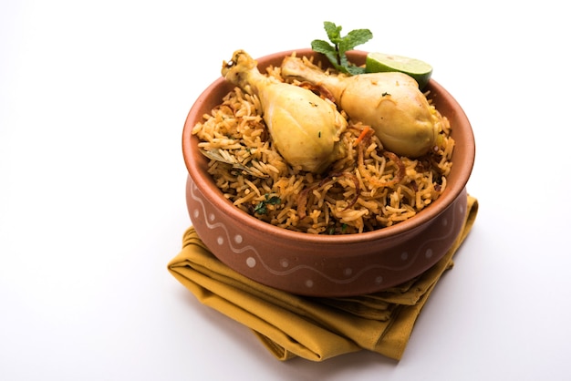 Indyjski kurczak Biryani podawany w misce z terakoty z jogurtem na białym tle. selektywne skupienie