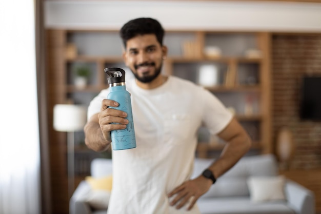 Indyjski mężczyzna z butelką wody pozuje przy żywym pokojem