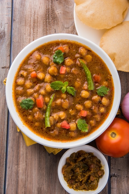 Indyjskie danie pikantne curry z ciecierzycy, znane również jako Chola lub Chana Masala lub powszechnie Chole, podawane ze smażonym puri lub poori na kolorowym lub drewnianym tle. Selektywne skupienie