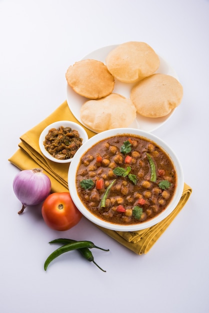 Indyjskie danie pikantne curry z ciecierzycy, znane również jako Chola lub Chana Masala lub powszechnie Chole, podawane ze smażonym puri lub poori na kolorowym lub drewnianym tle. Selektywne skupienie