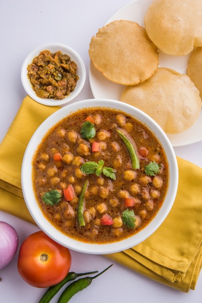 Indyjskie danie pikantne curry z ciecierzycy, znane również jako Chola lub Chana Masala lub powszechnie Chole, podawane ze smażonym puri lub poori na kolorowym lub drewnianym tle. Selektywne skupienie