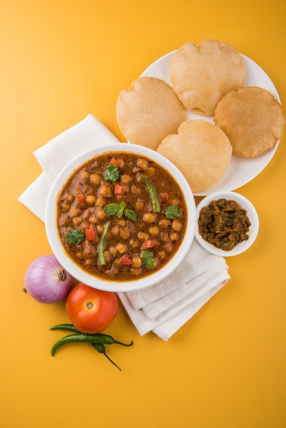 Indyjskie danie pikantne curry z ciecierzycy, znane również jako Chola lub Chana Masala lub powszechnie Chole, podawane ze smażonym puri lub poori na kolorowym lub drewnianym tle. Selektywne skupienie