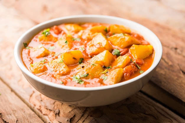 Indyjskie jedzenie - Aloo curry masala. Ziemniak gotowany z przyprawami i ziołami w pomidorowym curry. podawane w misce na nastrojowym tle. selektywne skupienie