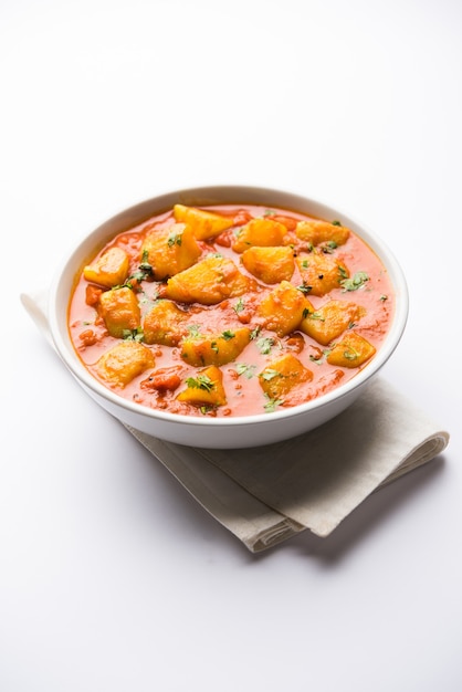 Indyjskie jedzenie - Aloo curry masala. Ziemniak gotowany z przyprawami i ziołami w pomidorowym curry. podawane w misce na nastrojowym tle. selektywne skupienie