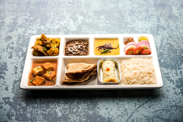 Indyjskie jedzenie wegetariańskie Taca Thali lub Parcel z przegródkami, w której podawana jest paneer, dal makhani lub parka, aloo-gobi sabji, chapati i ryż z bengalskim słodkości