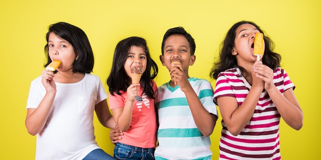 Indyjskie lub azjatyckie słodkie małe dzieci jedzące lody lub batoniki mango lub cukierki. Na białym tle nad kolorowym tłem