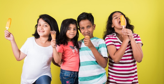 Indyjskie lub azjatyckie słodkie małe dzieci jedzące lody lub batoniki mango lub cukierki. Na białym tle nad kolorowym tłem