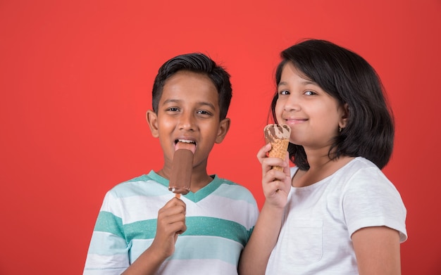 Indyjskie lub azjatyckie słodkie małe dzieci jedzące lody lub batoniki mango lub cukierki. Na białym tle nad kolorowym tłem