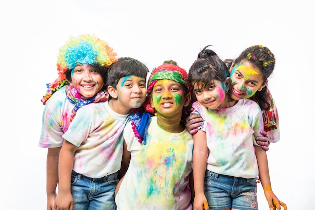 Indyjskie małe dzieci, przyjaciele lub rodzeństwo świętujące święto Holi z kolorem gulal lub proszku, słodyczami, pichkari lub sprayem, odizolowane na białym tle
