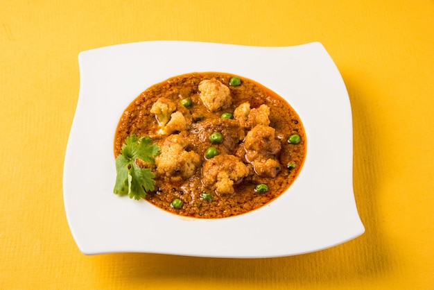 Indyjskie pikantne jedzenie Gobi Masala lub curry z kalafiora z zielonym groszkiem, podawane w ceramicznej misce, selektywne focus