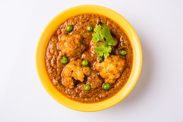 Indyjskie pikantne jedzenie Gobi Masala lub curry z kalafiora z zielonym groszkiem, podawane w ceramicznej misce, selektywne focus