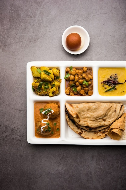 Indyjskie wegetariańskie jedzenie Thali lub Parcel taca z przegródkami, w której podawane są Malai Kofta, chole, Dal tarka, suchy aloo sabji, chapati i ryż ze słodkim gulab jamun