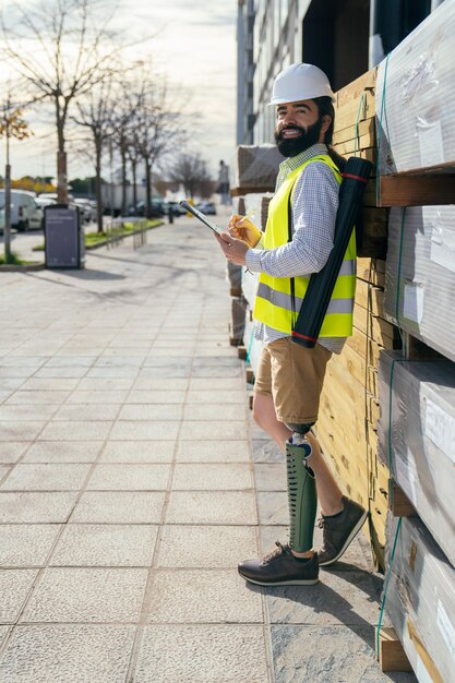 Inspektor w kamizelce highvis i hełmie z notatką na schowku z widoczną wysokiej technologii protezą nogi