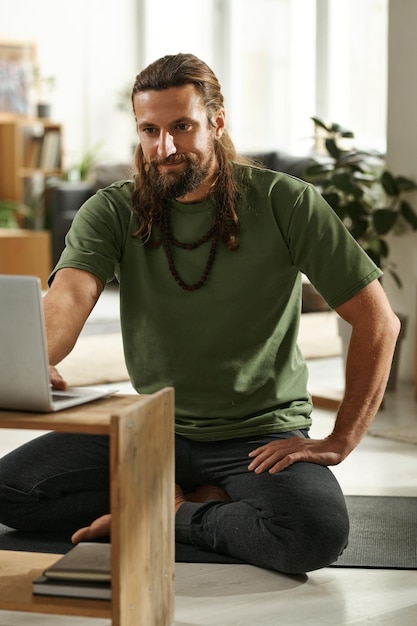 Instruktor jogi siedzi na podłodze przed laptopem i rozmawia ze swoimi uczniami online