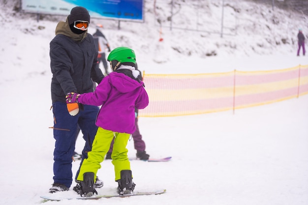 Instruktorzy uczą jeździć na snowboardzie dziecko na stoku śnieżnym