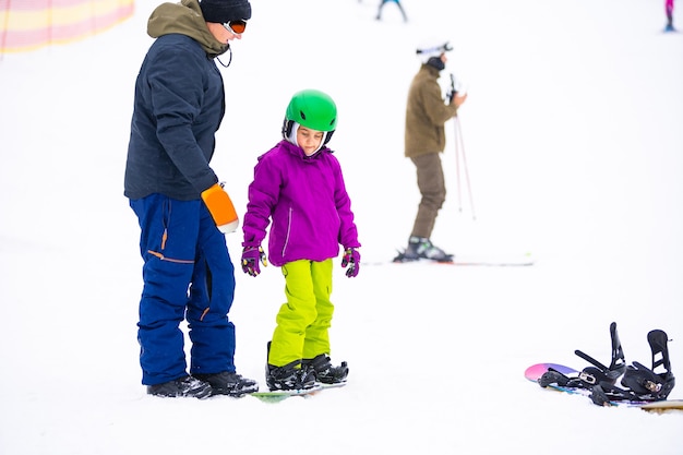 Instruktorzy uczą jeździć na snowboardzie dziecko na stoku śnieżnym