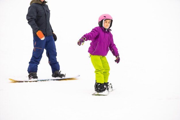 Instruktorzy uczą jeździć na snowboardzie dziecko na stoku śnieżnym